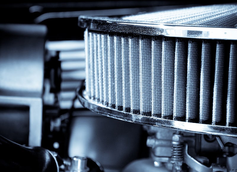 Close-up of a cylindrical high-performance engine air filter with a metallic mesh element installed in a vehicle engine compartment